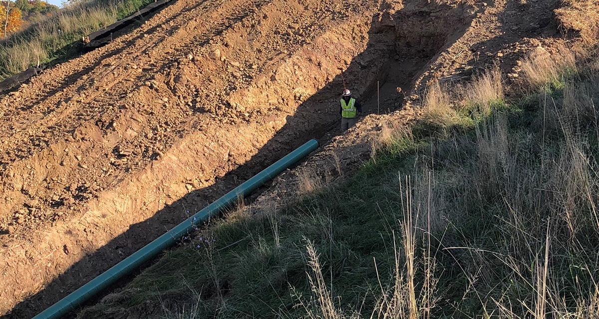 There is an Equitrans employee monitoring work inside a pipeline trench.