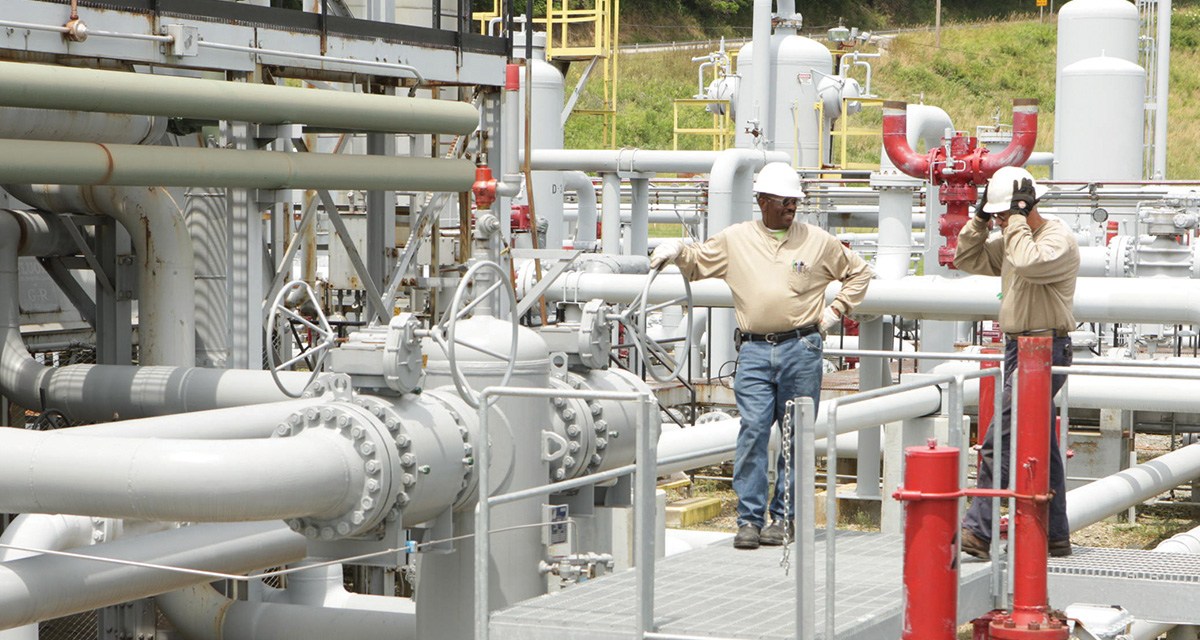 Two Equitrans employees are on an elevated platform surrounded by operating pipelines.