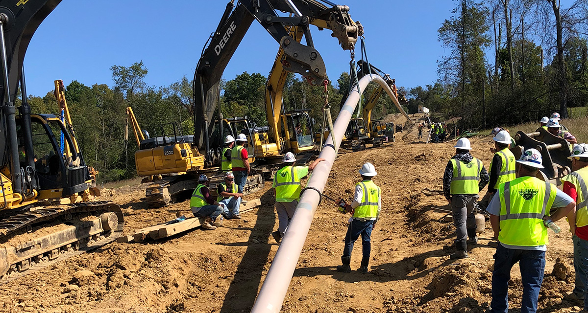  Three Equitrans employees wearing their PPE are standing on an outdoor Equitrans site next to an above-ground pipeline.