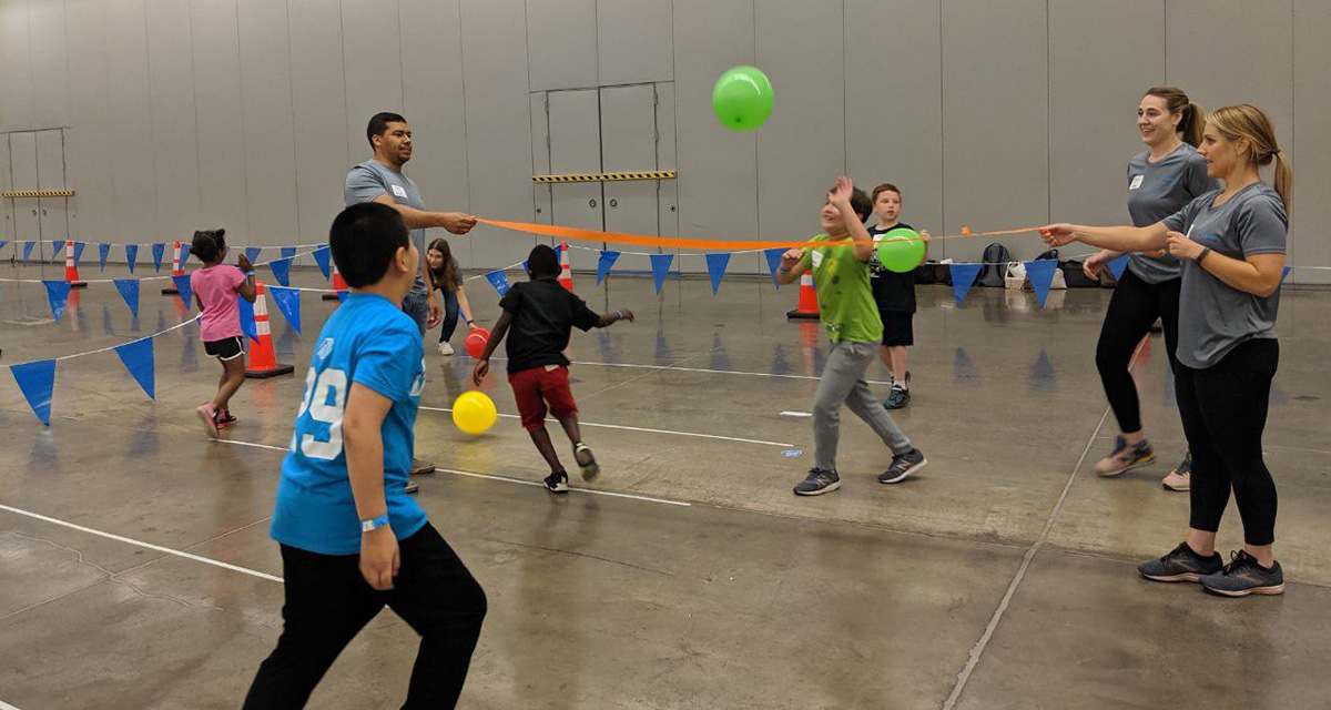 Three Equitrans employees are volunteering at a community inclusion event playing with balloons in a gymnasium.