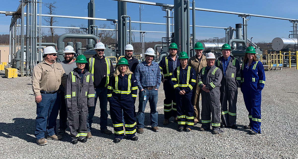 A large group of Equitrans employees on a work site wearing their Personal Protective Equipment (PPE), including safety glasses, vests, hard hats, and hard-toed boots.