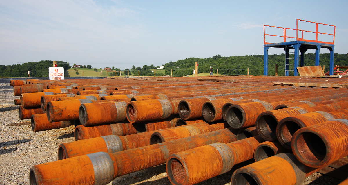 There are a dozen stacked pipeline segments on an Equitrans outdoor worksite.