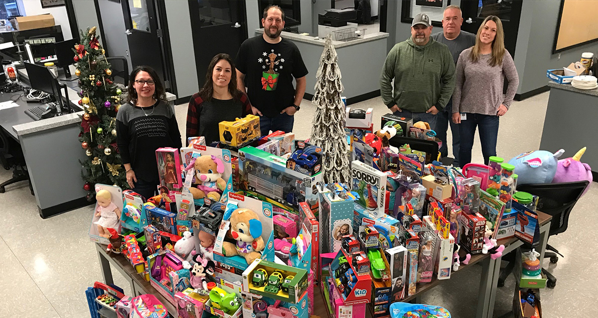 Six Equitrans employees are surrounding an office table covered in Toys-for-Tots donations.