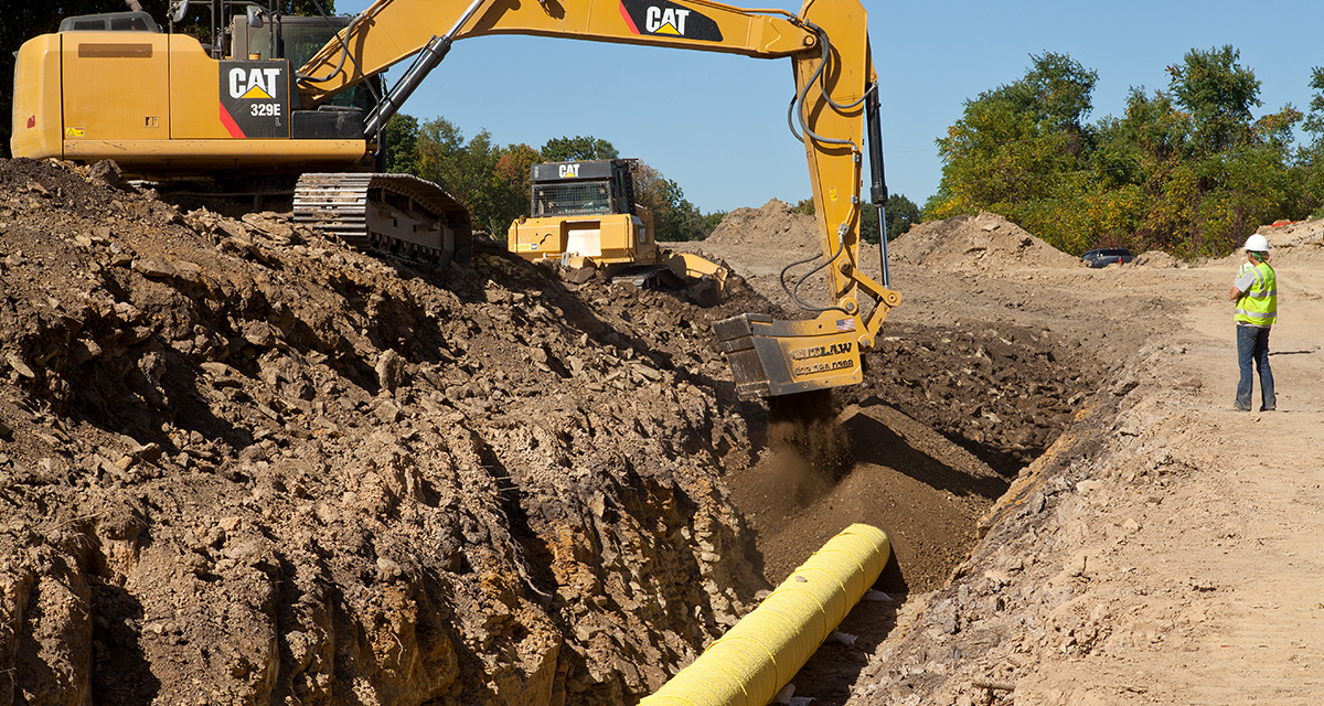 An excavator fills in soil on top of an installed pipeline.