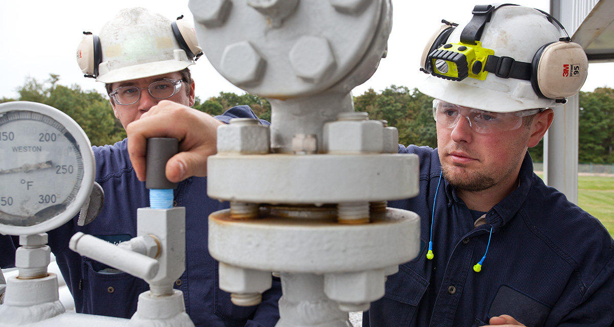 Two Equitrans employees are wearing PPE inspecting a gauge connected to an above-ground pipeline.