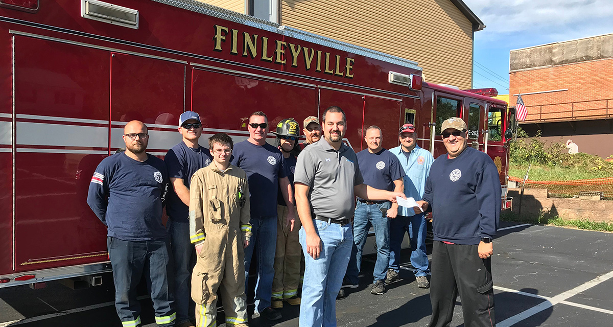 Equitrans employees are standing with a group of Finleyville first responders in front of a fire truck.