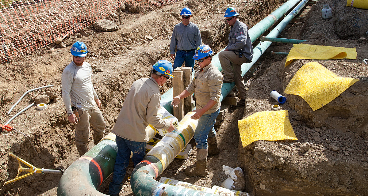 Five Equitrans employees are wearing PPE while assembling a pipeline in a shallow trench at a construction site.