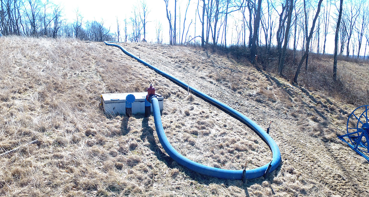 An on-surface blue water hose is connecting to an unground pipeline.